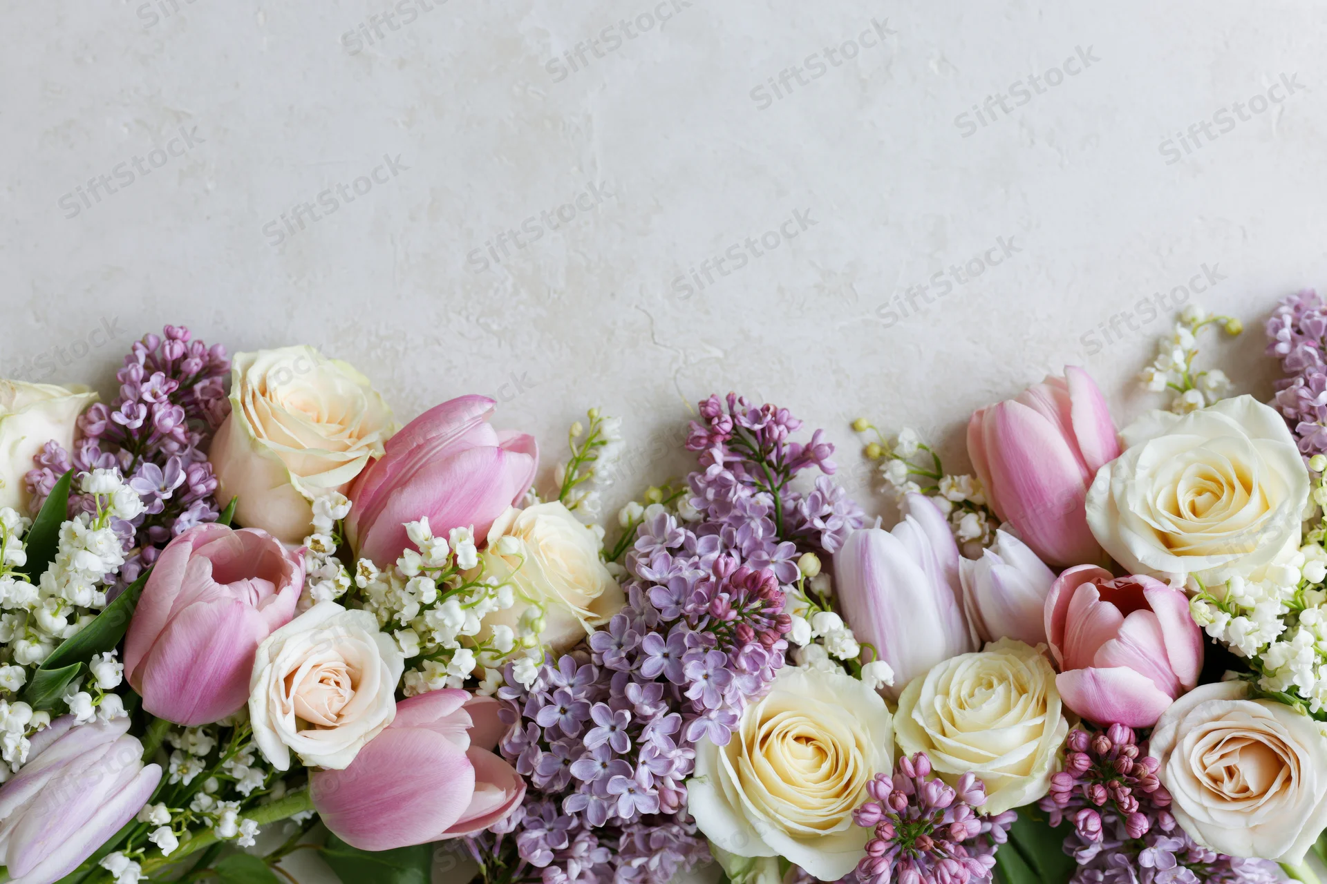 Spring bouquet of roses, tulips and lilacs arranged along bottom edge with copyspace above