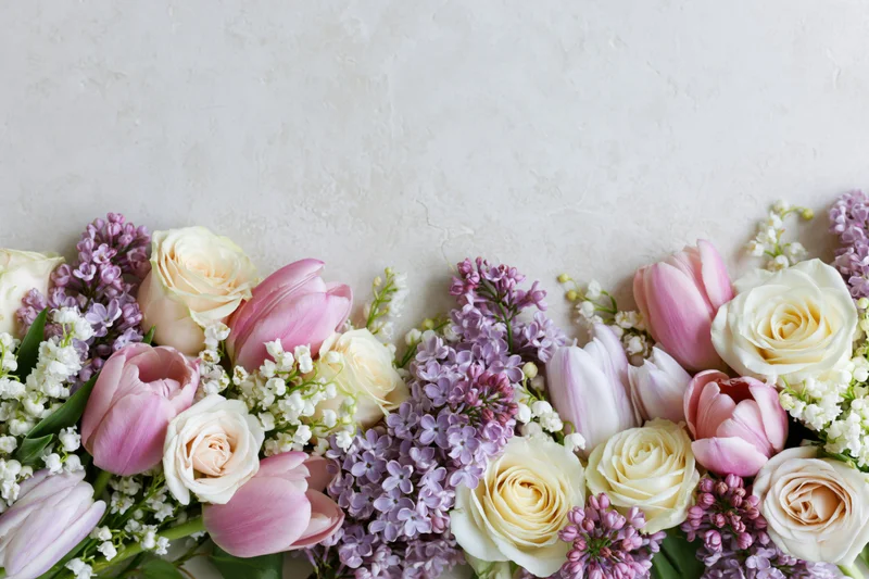 Spring bouquet of roses, tulips and lilacs arranged along bottom edge with copyspace above