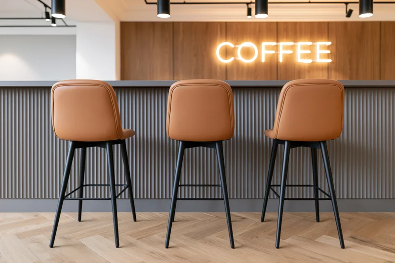 Three tan upholstered bar stools at a modern coffee shop counter with neon sign and ribbed paneling