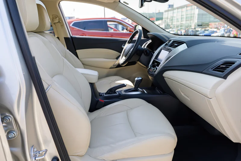 Interior of a modern compact SUV viewed from open passenger side door showing beige leather seats and dashboard controls