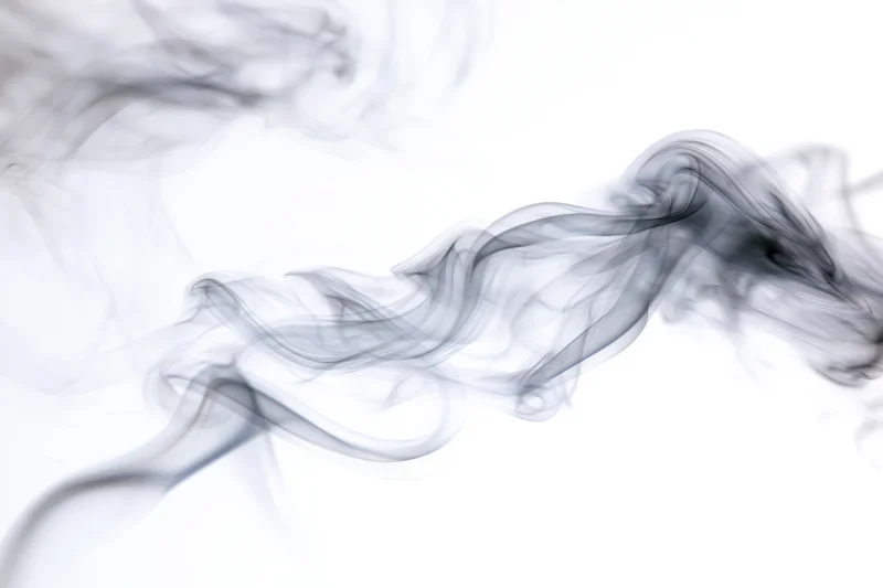Dark smoke rising and curling in thin wisps against a white background