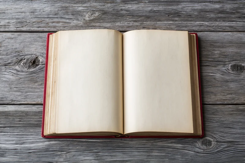 Open hardcover book with blank cream pages lying flat on weathered gray wooden surface