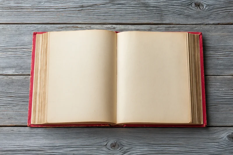 Open hardcover book with blank pages lying flat on weathered gray wooden surface