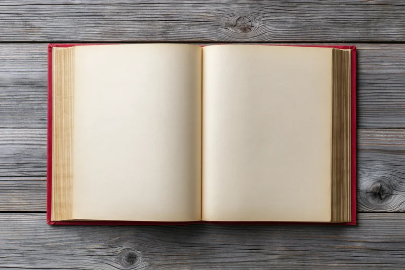 Open hardcover book with blank pages lying flat on weathered wooden surface