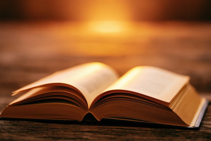 Open hardcover book lying flat on a worn wooden table with warm ambient light glowing on the pages