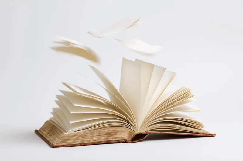 Open hardcover book with pages flying and scattered on white background