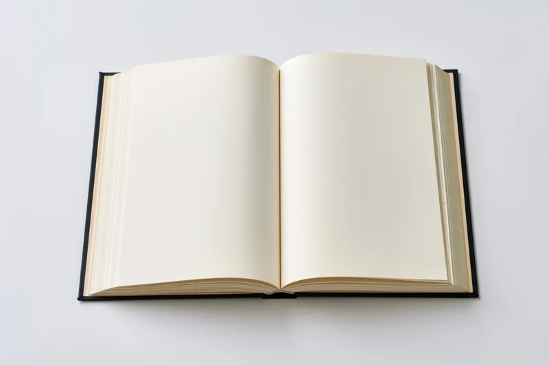 Open hardcover book with blank cream pages lying flat on white background