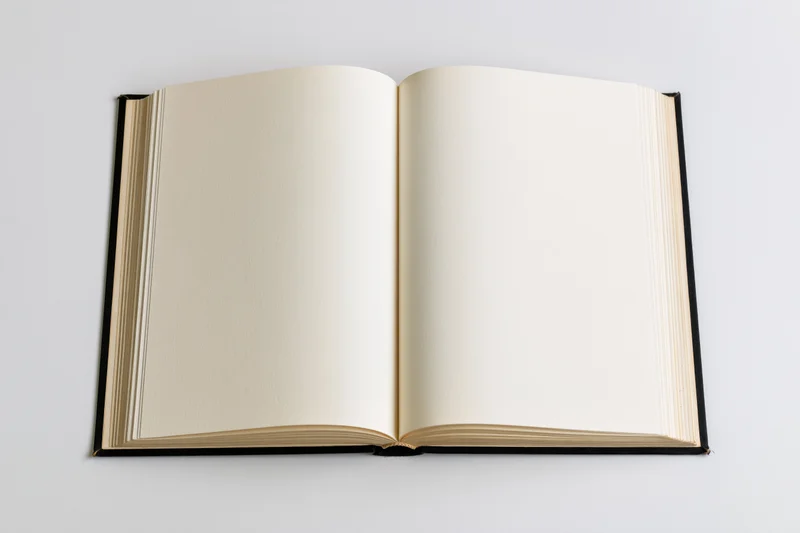 Open hardcover book with blank cream pages lying flat spread on white background