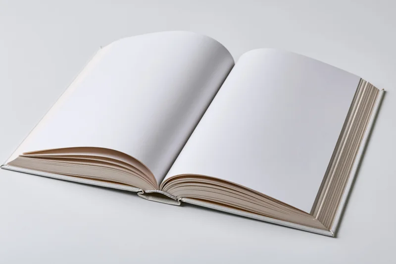 Open hardcover book with blank white pages spread flat on white surface