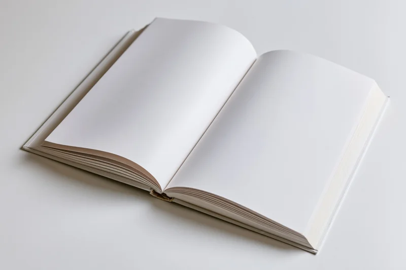 Open hardcover book with blank white pages spread flat on white surface