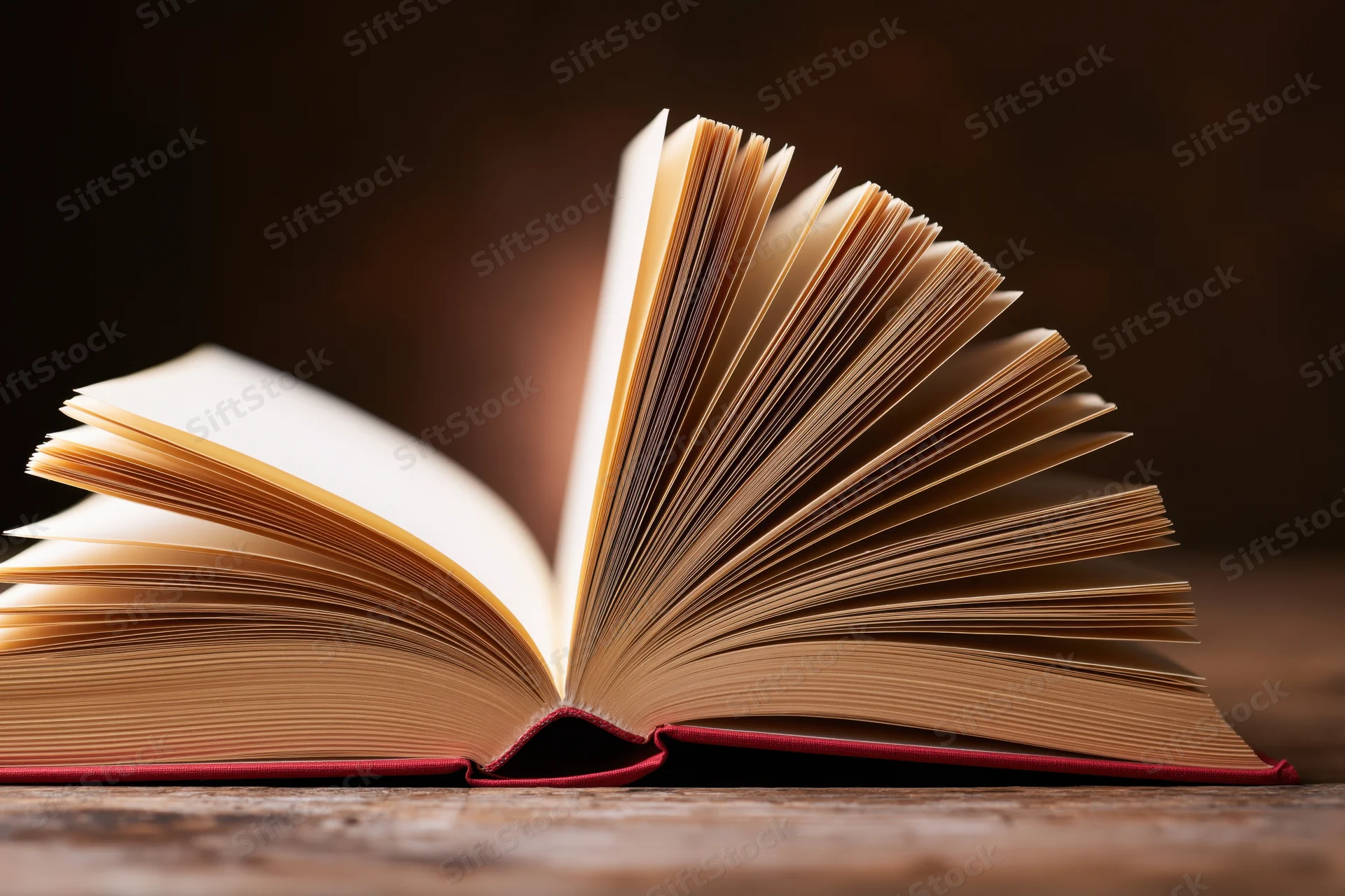 Open hardcover book with fanned pages resting on a worn wooden surface