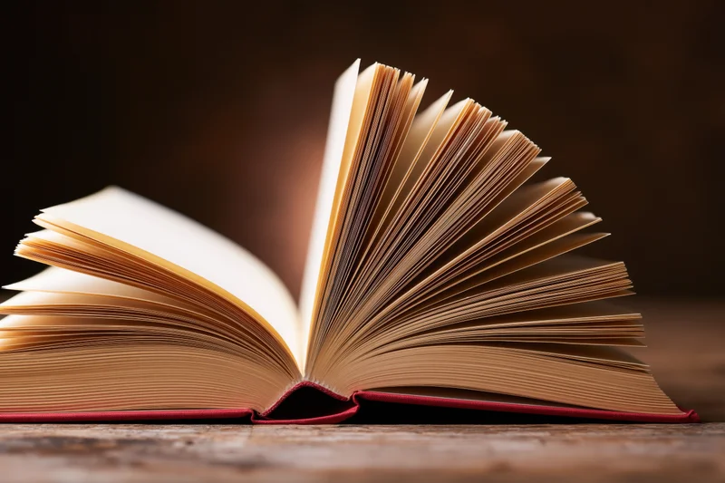 Open hardcover book with fanned pages resting on a worn wooden surface