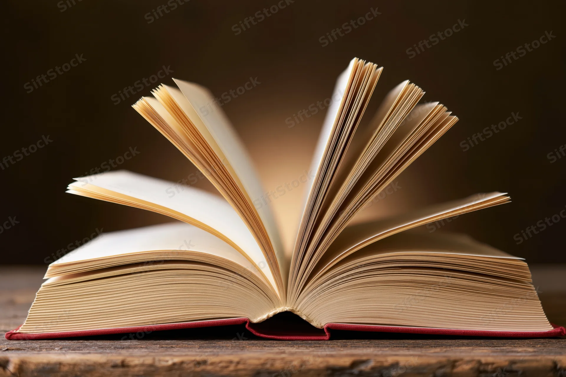 Open hardcover book with fanned pages resting on a worn wooden table
