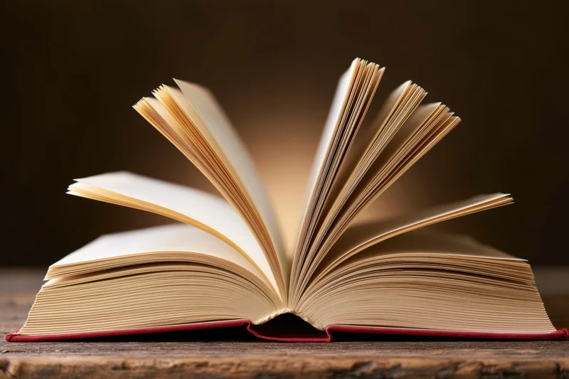 Open hardcover book with fanned pages resting on a worn wooden table
