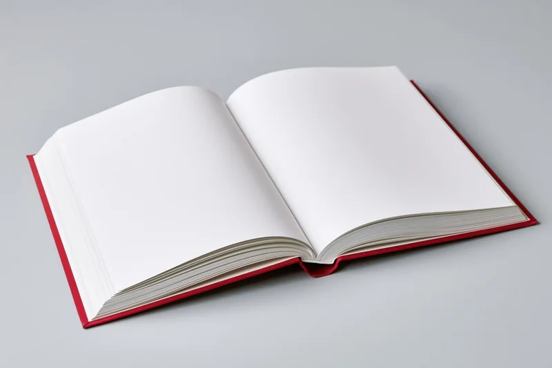 Open hardcover book with red binding and blank white pages on gray surface