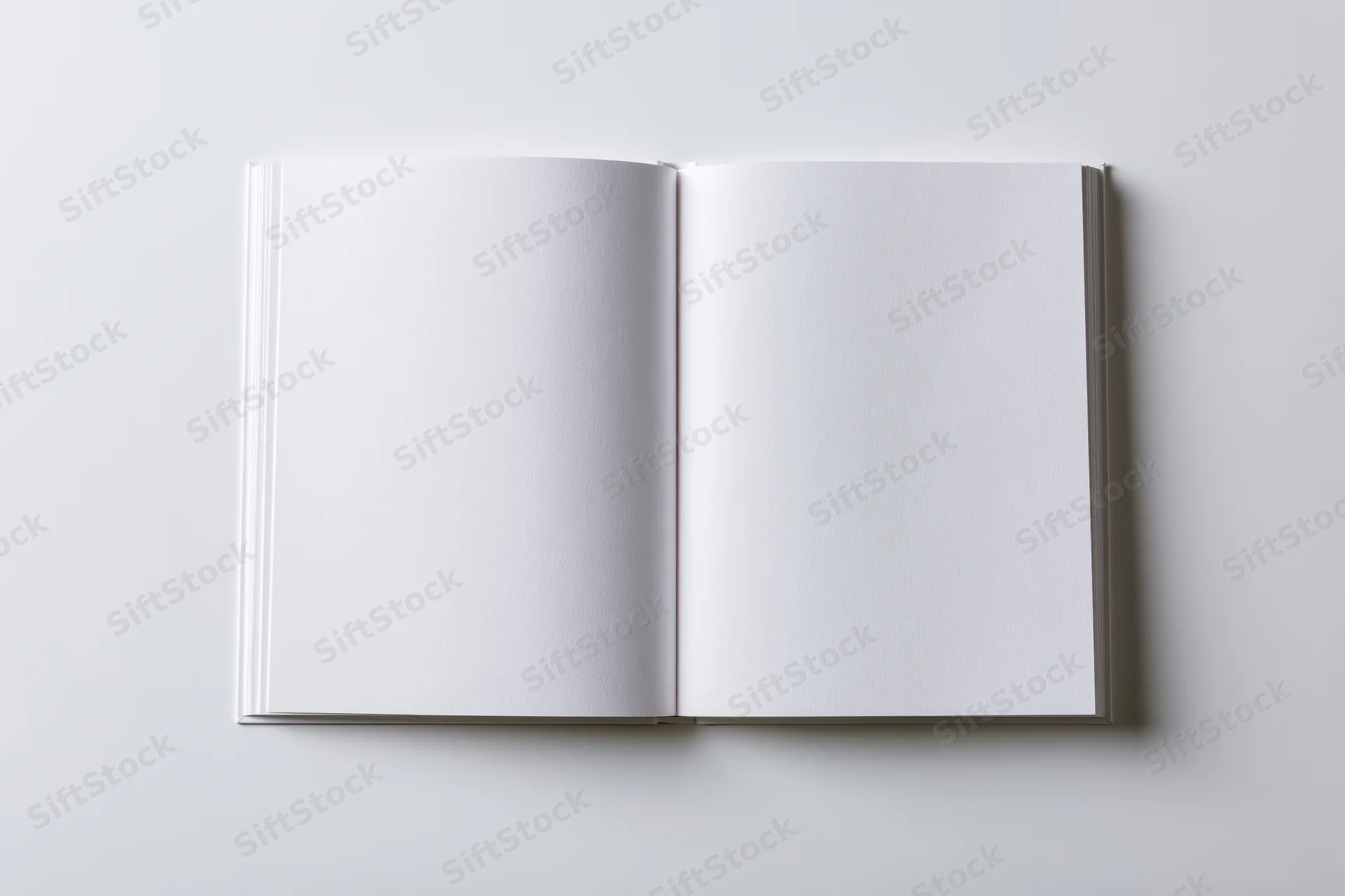 Open square hardcover book lying flat with blank white pages on white surface