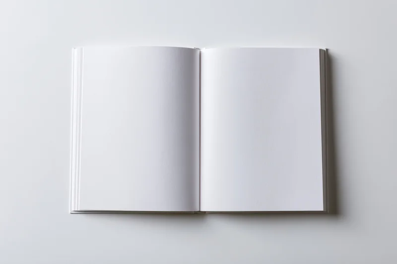 Open square hardcover book lying flat with blank white pages on white surface