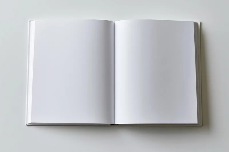 Open hardcover book with blank white pages lying flat on a plain surface