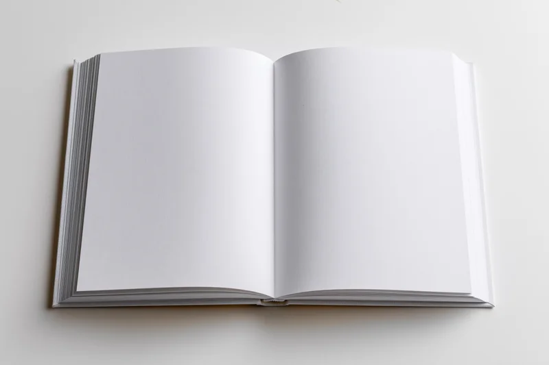 Open hardcover book with blank white pages on white surface