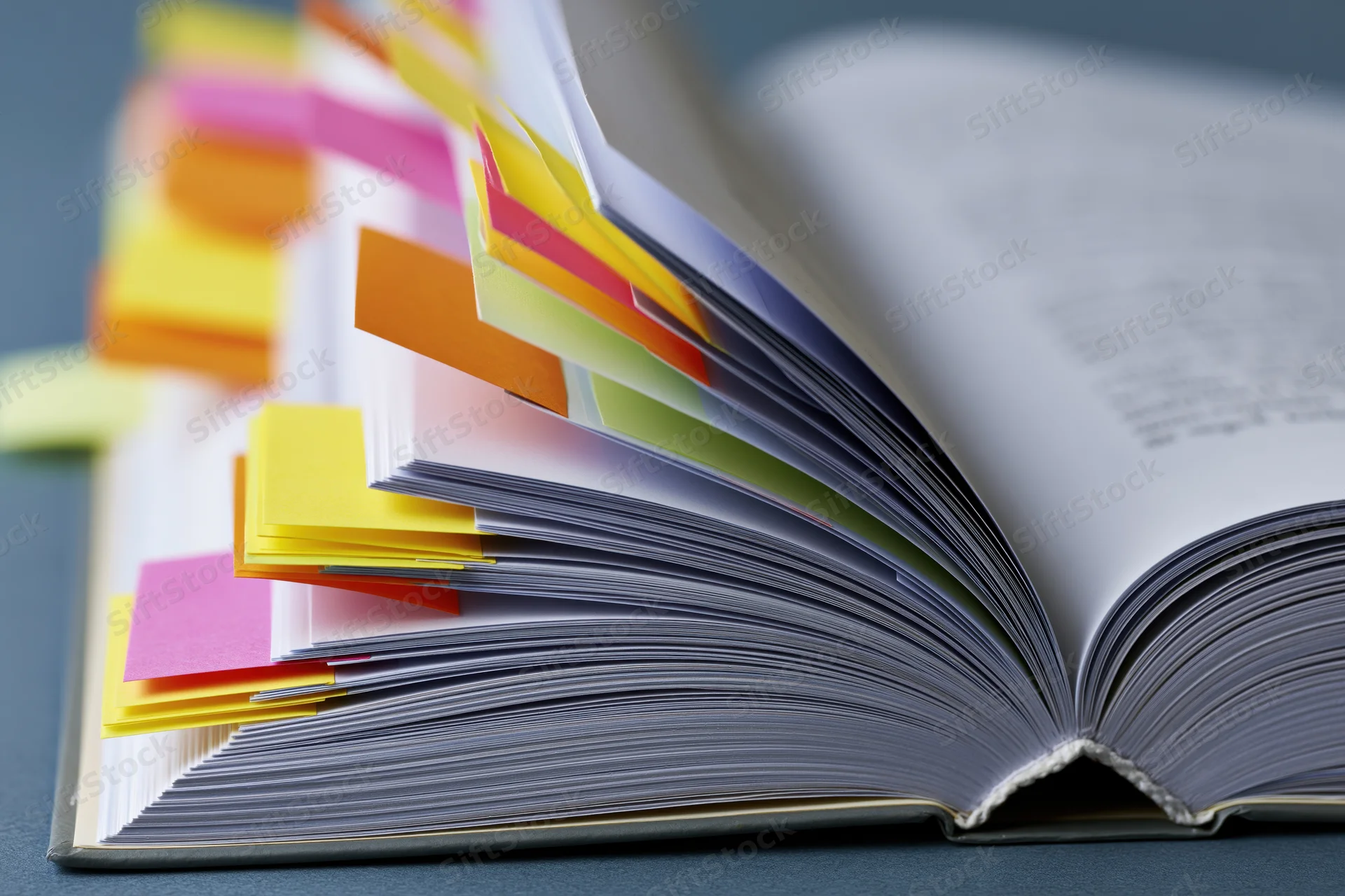 Open thick book with colorful sticky notes marking pages on a gray surface