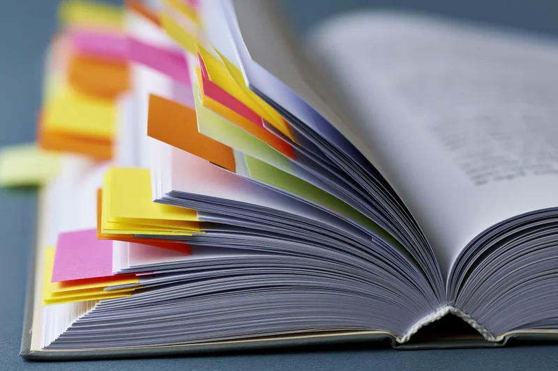 Open thick book with colorful sticky notes marking pages on a gray surface