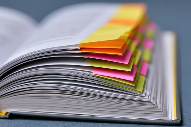 Open book with fanned pages and colorful sticky notes on gray surface