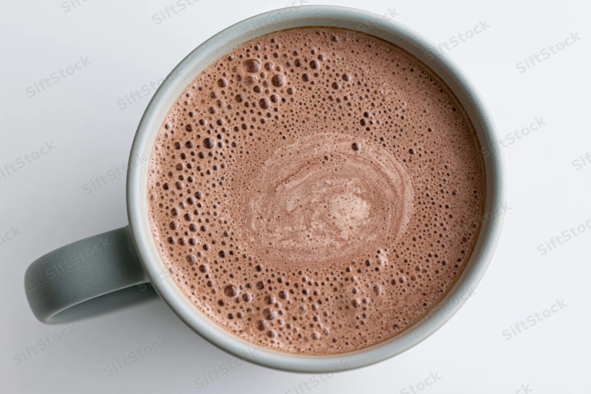 Overhead view of a grey ceramic mug filled with frothy hot chocolate, showing bubbles and swirl on white background