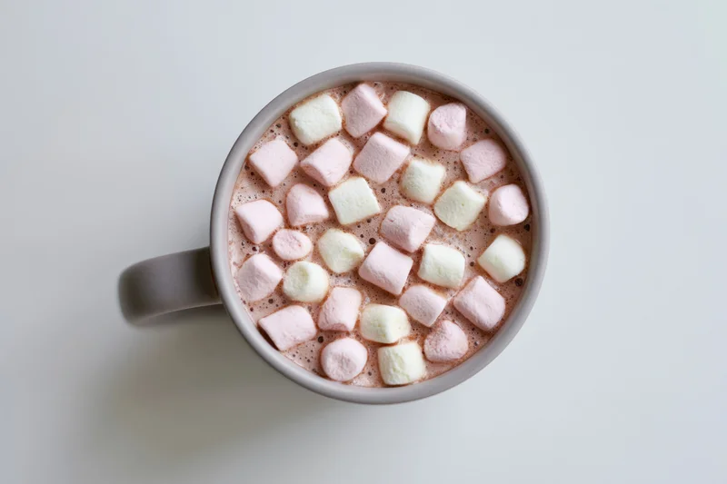 Overhead view of a grey ceramic mug filled with hot chocolate and topped with pink and white marshmallows on a white surface