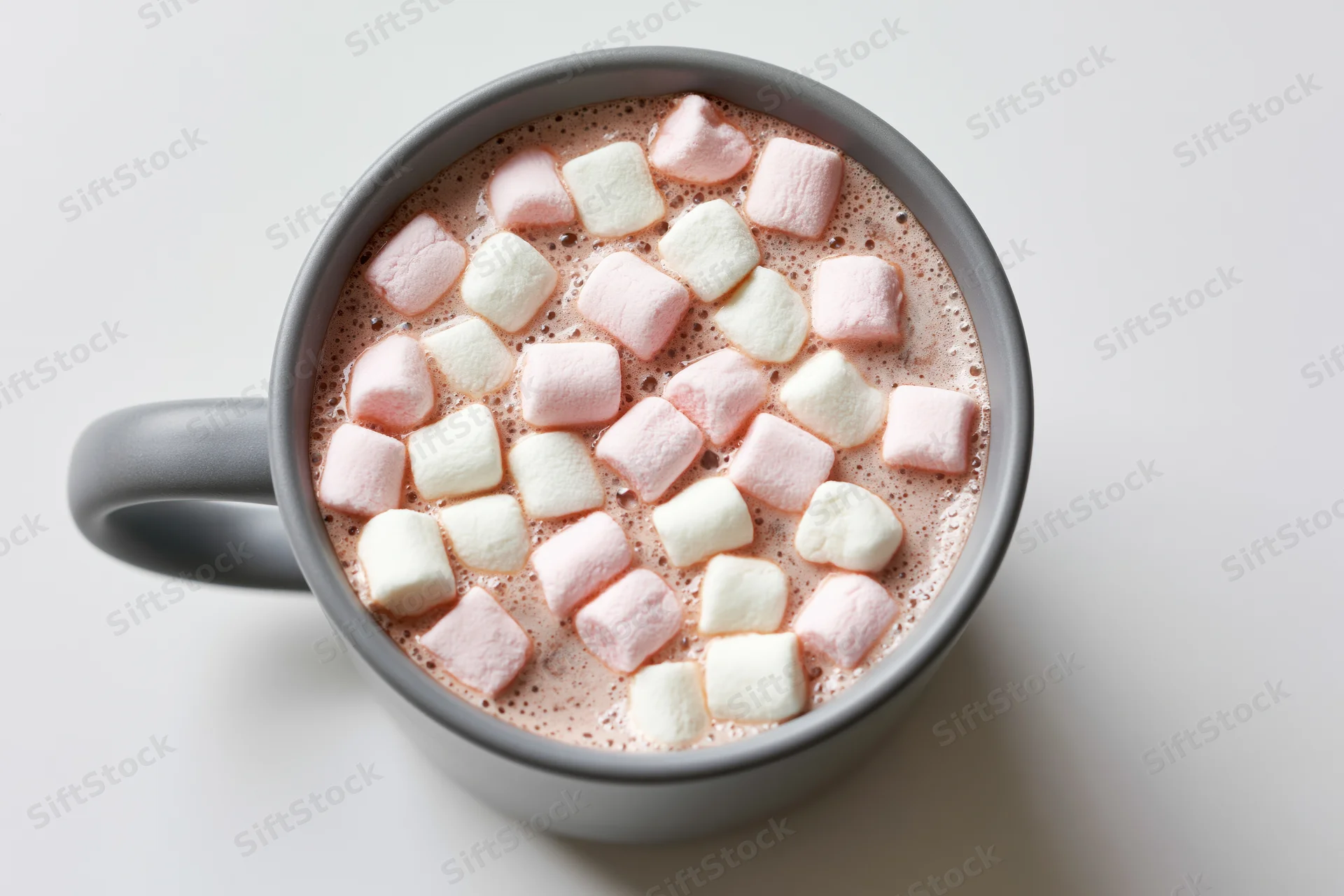 Overhead view of a grey ceramic mug filled with hot chocolate and floating pink and white marshmallows on a plain white surface