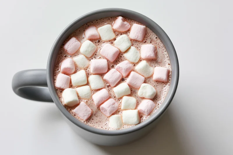 Overhead view of a grey ceramic mug filled with hot chocolate and floating pink and white marshmallows on a plain white surface