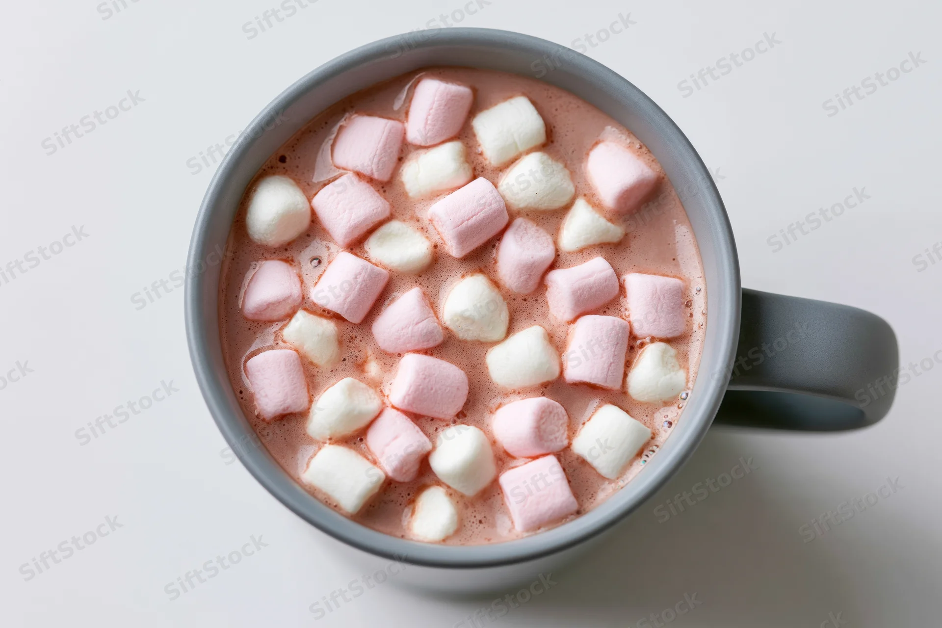 Overhead view of a grey ceramic mug filled with hot chocolate and floating pink and white marshmallows on a white surface