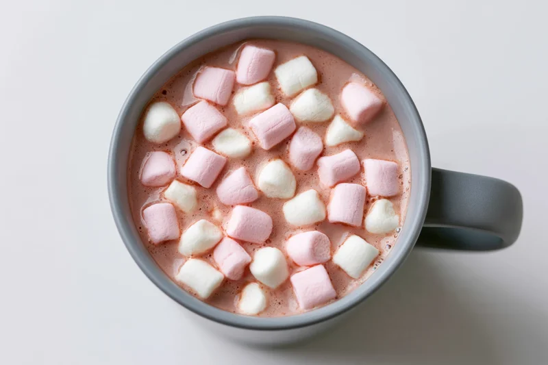 Overhead view of a grey ceramic mug filled with hot chocolate and floating pink and white marshmallows on a white surface