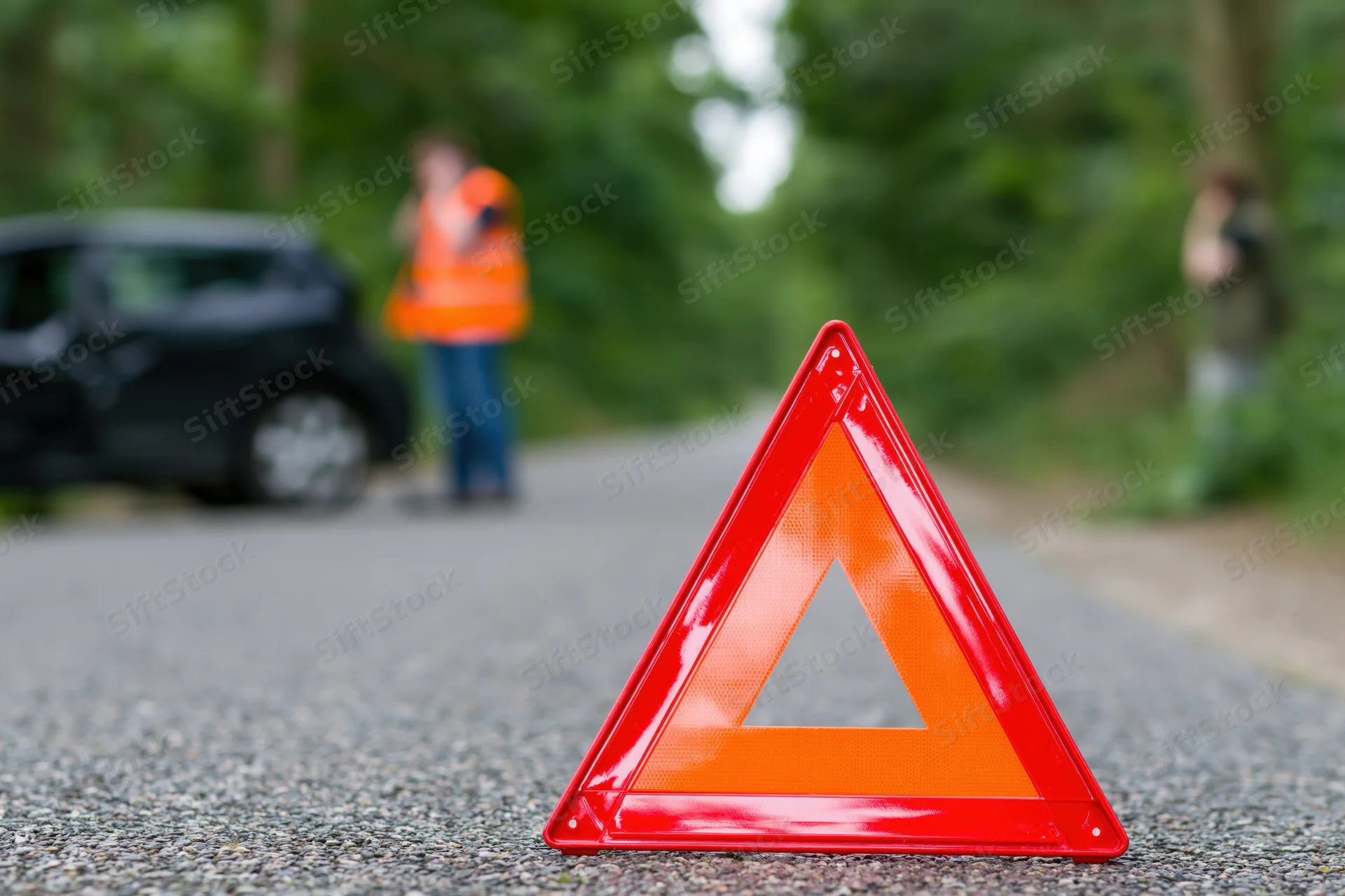 Red emergency warning triangle on asphalt road with blurred car and people in background