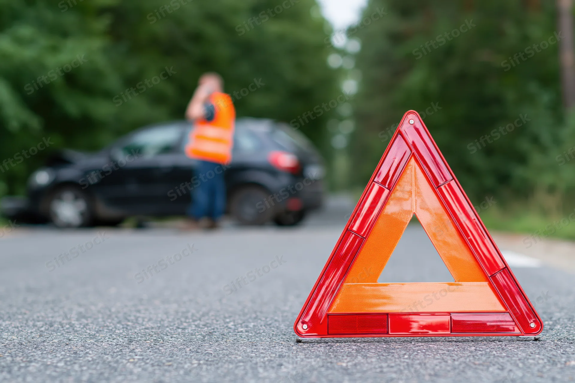 Red emergency warning triangle on asphalt road with car and driver in background