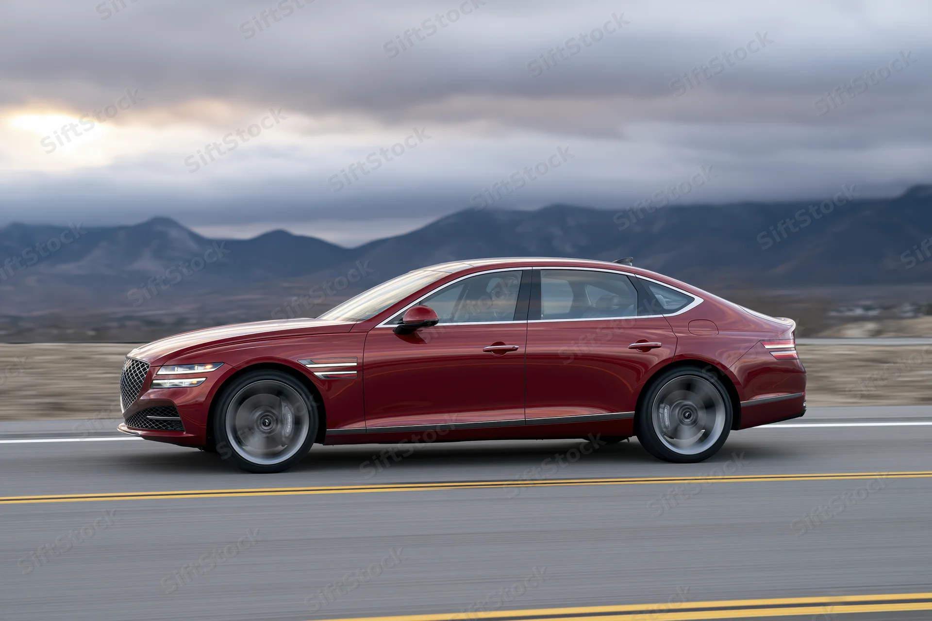 Red luxury sedan driving on a two-lane highway with mountains in the background