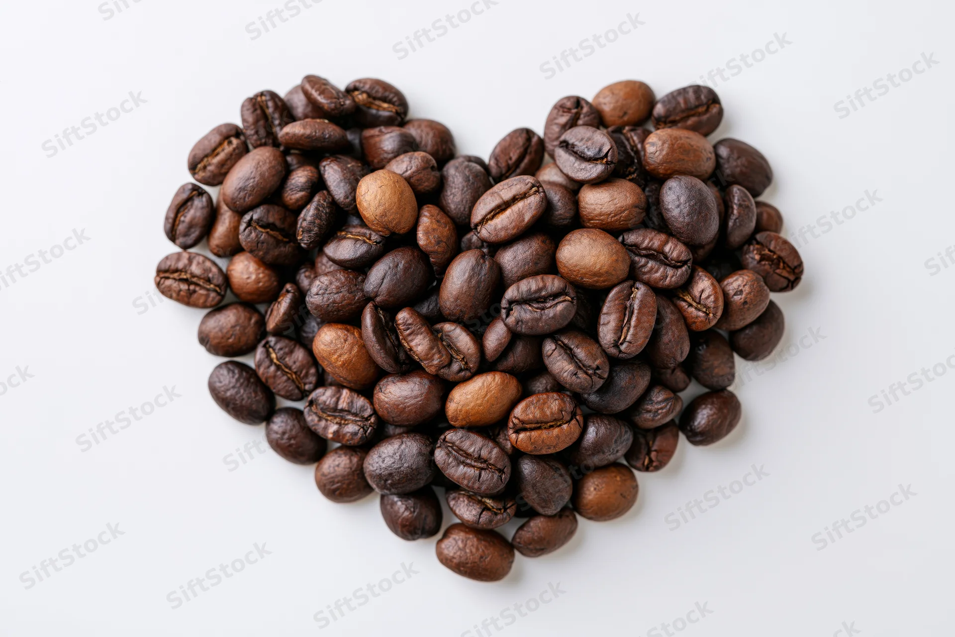 Roasted coffee beans arranged in heart shape on white background