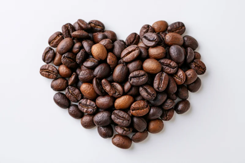 Roasted coffee beans arranged in heart shape on white background