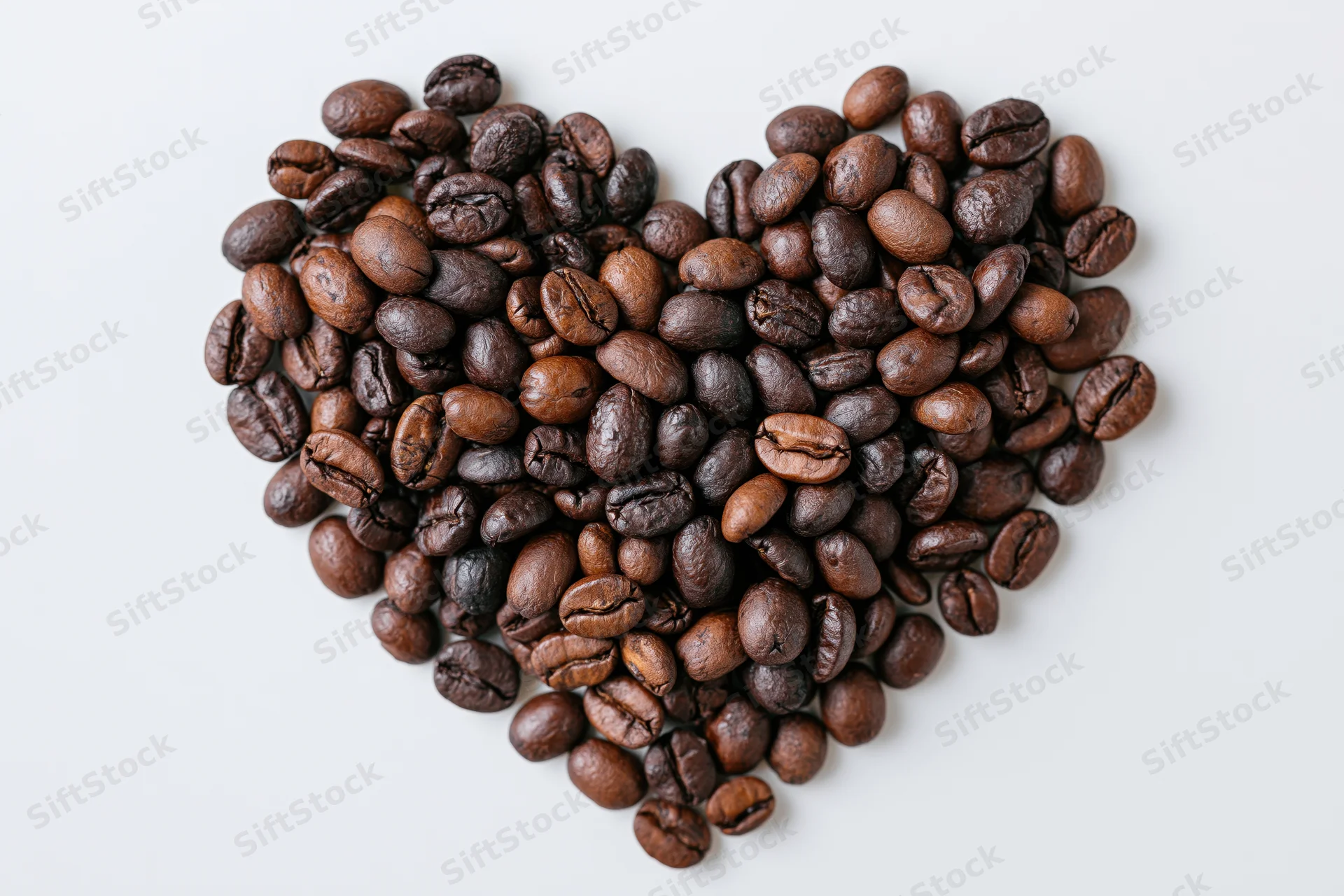 Roasted coffee beans arranged in heart shape on white background