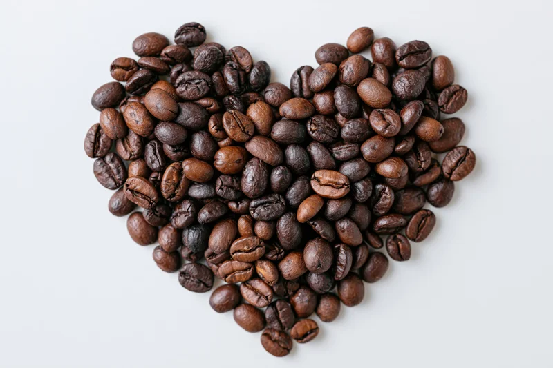 Roasted coffee beans arranged in heart shape on white background