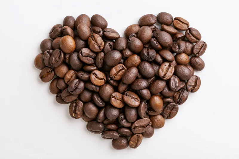 Roasted coffee beans arranged in heart shape on white background