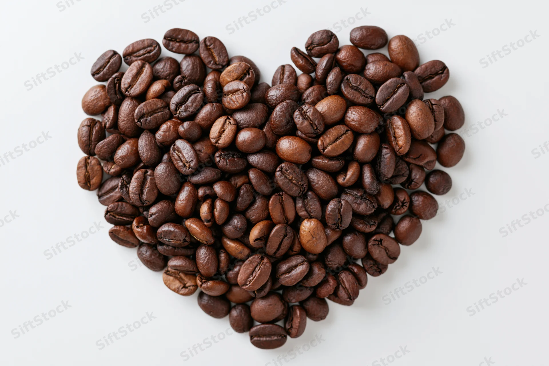Roasted coffee beans arranged in heart shape on white background