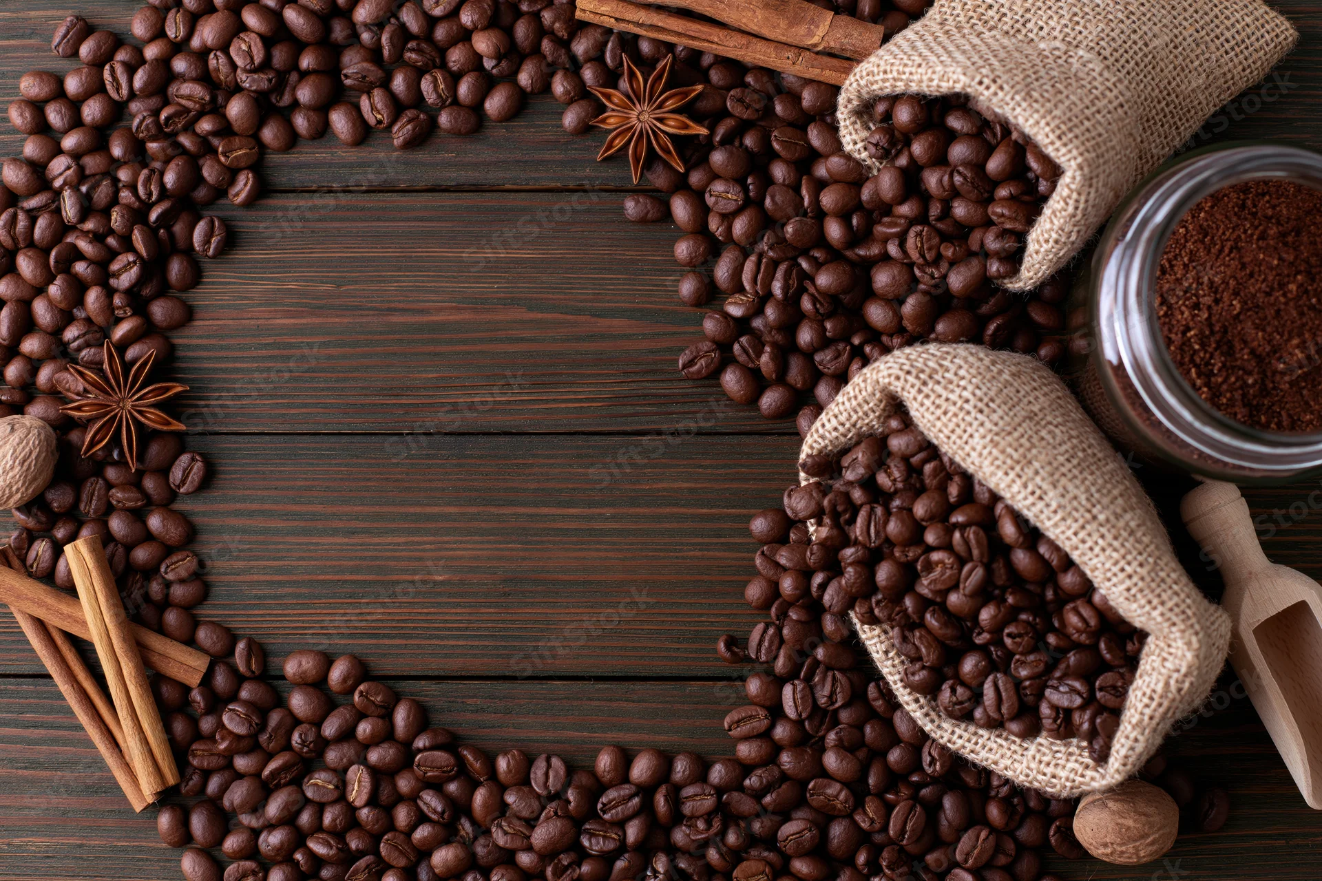 Roasted coffee beans arranged in a frame on dark wooden surface with spices and burlap sacks