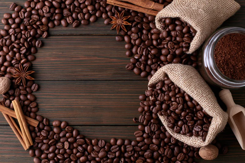Roasted coffee beans arranged in a frame on dark wooden surface with spices and burlap sacks