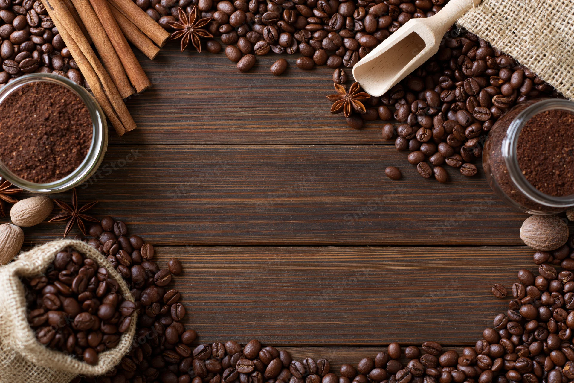 Roasted coffee beans and spices arranged in a frame on dark wooden surface with copyspace in center