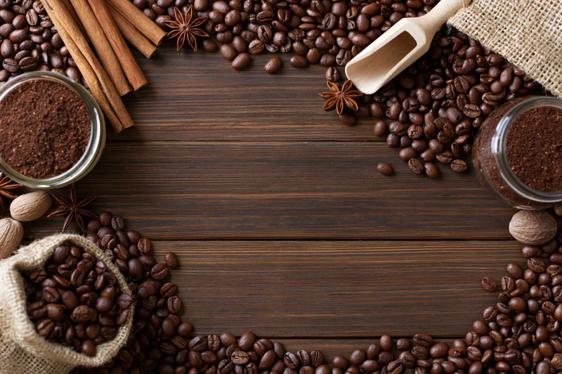 Roasted coffee beans and spices arranged in a frame on dark wooden surface with copyspace in center