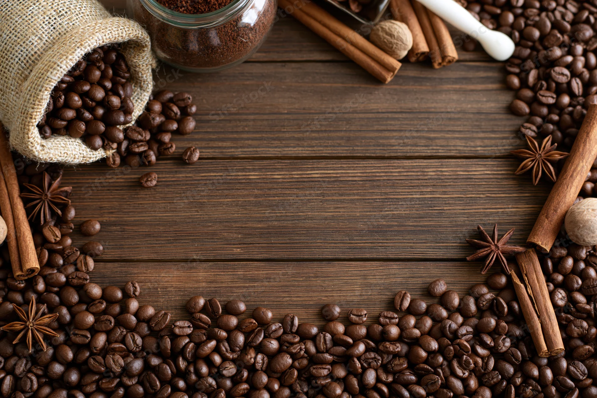 Roasted coffee beans and spices arranged in a frame on a dark wooden surface with copyspace in the center