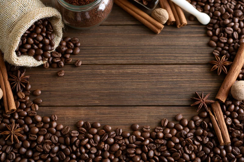 Roasted coffee beans and spices arranged in a frame on a dark wooden surface with copyspace in the center