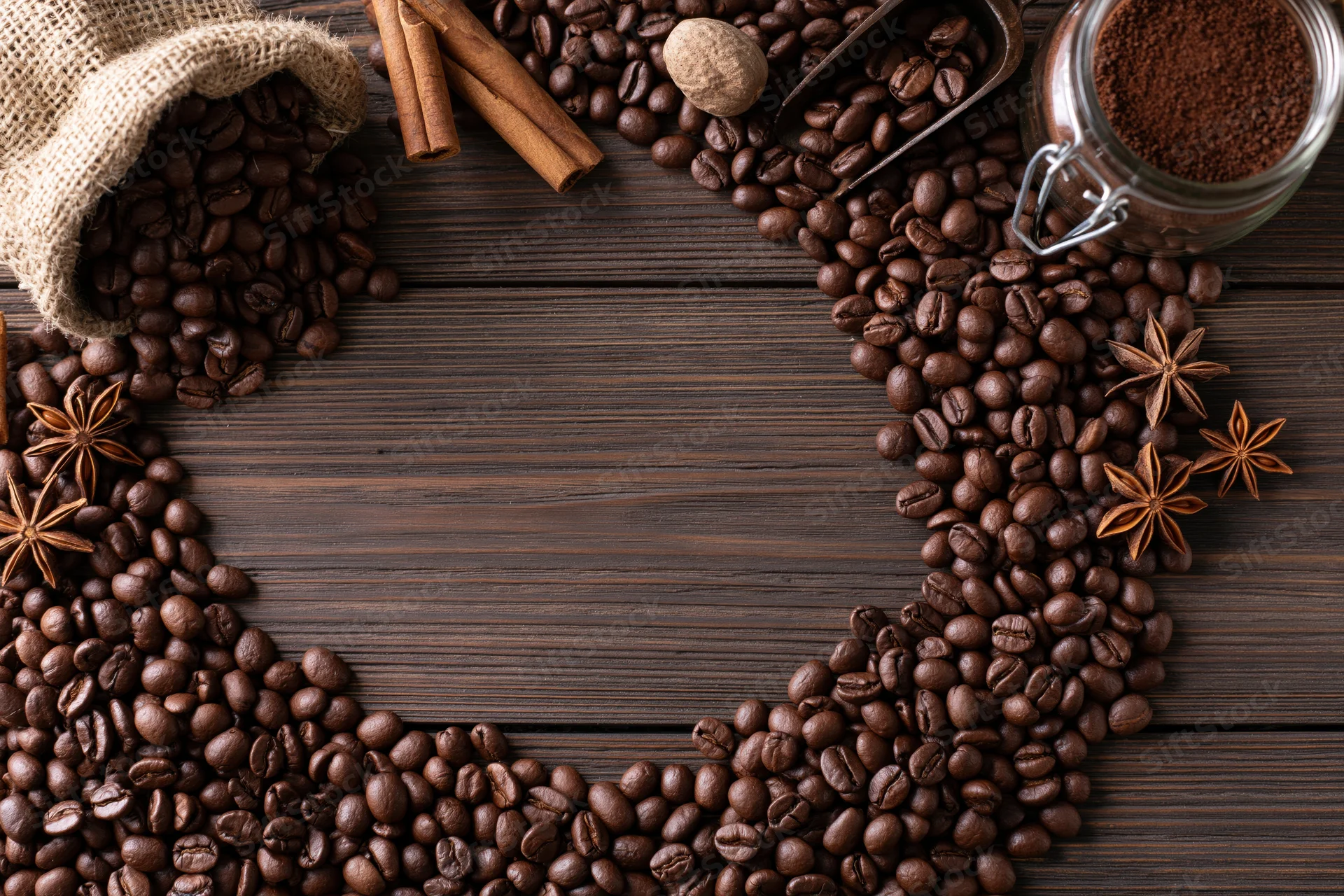Coffee beans arranged in heart shape on dark wooden table with spices and jar of ground coffee