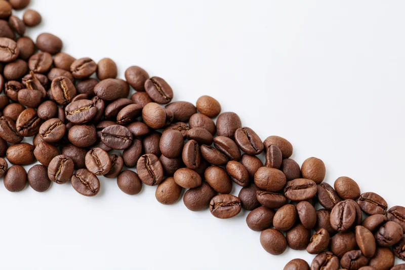 Roasted coffee beans scattered across white background with copyspace