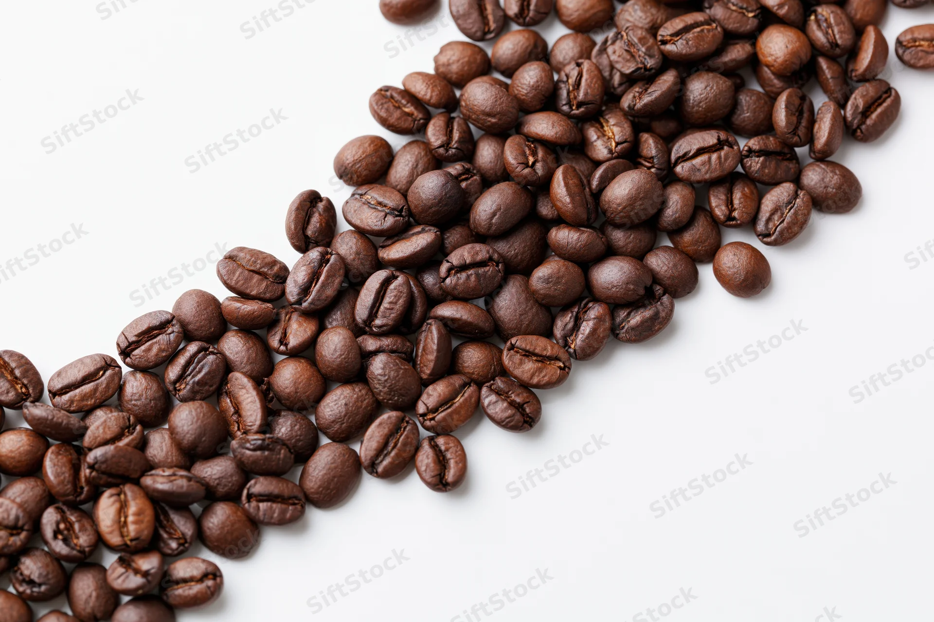Roasted coffee beans scattered across white surface with copyspace